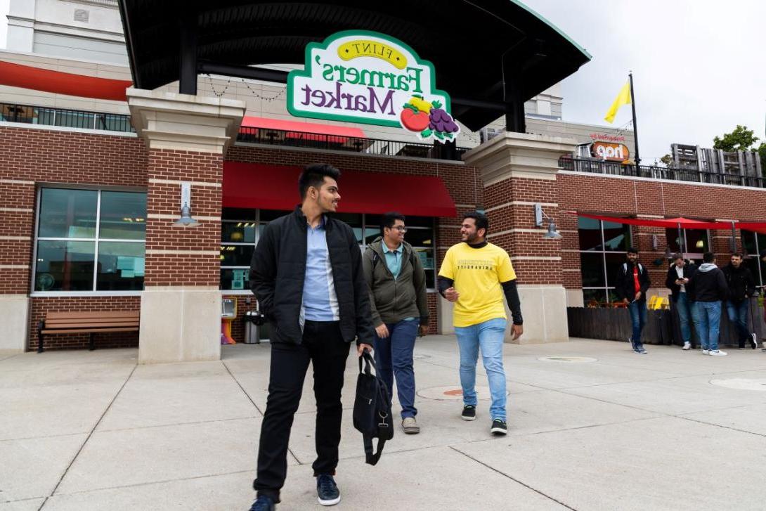 Three students walk outside the entrance of the Flint Farmers' Market